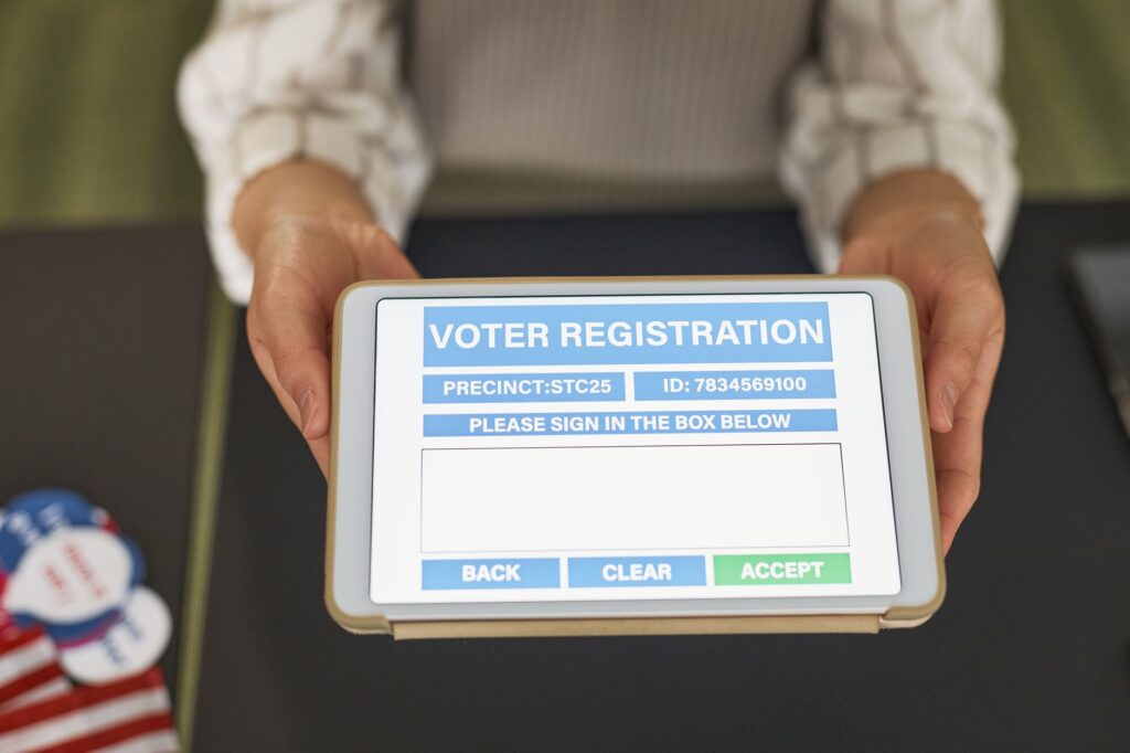 Mãos segurando tablet com consulta digital de eleitor em seção de votação