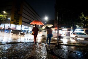 Pedestres com guarda-chuvas caminhando em rua urbana na chuva